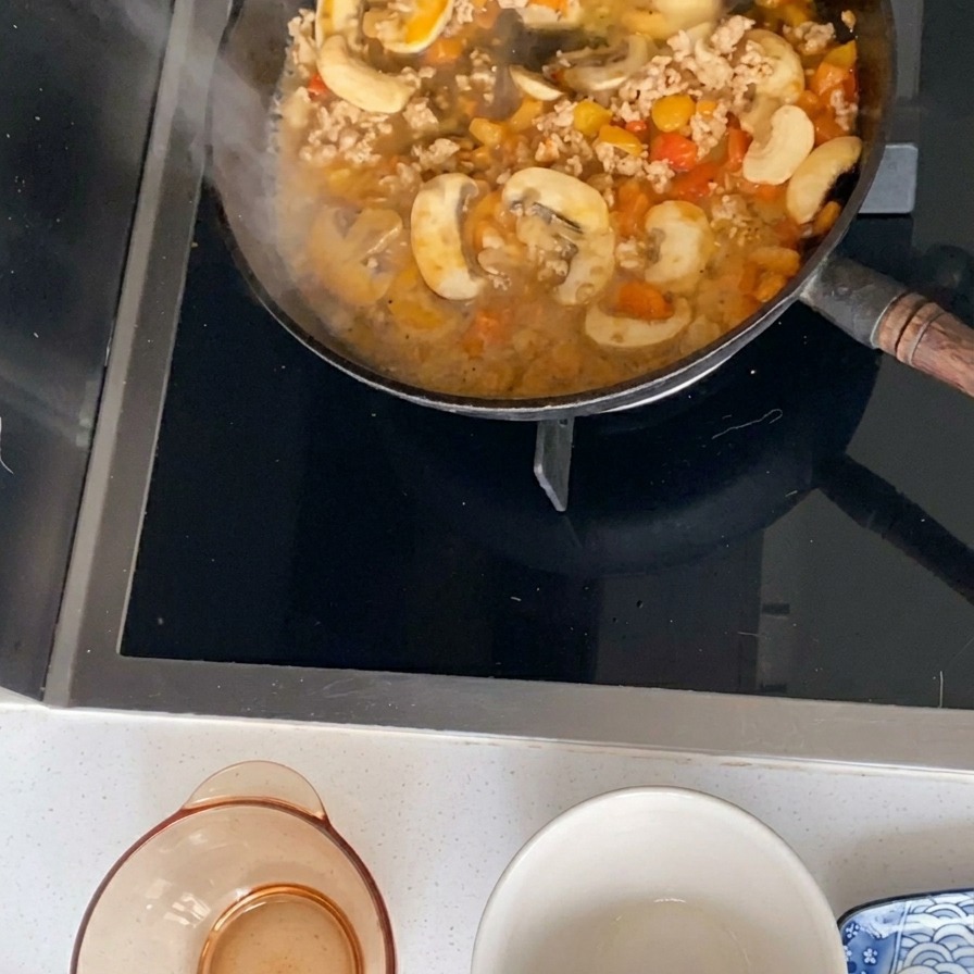 Una salsa de cerdo, champiñones y tomates hirviendo en una sartén.