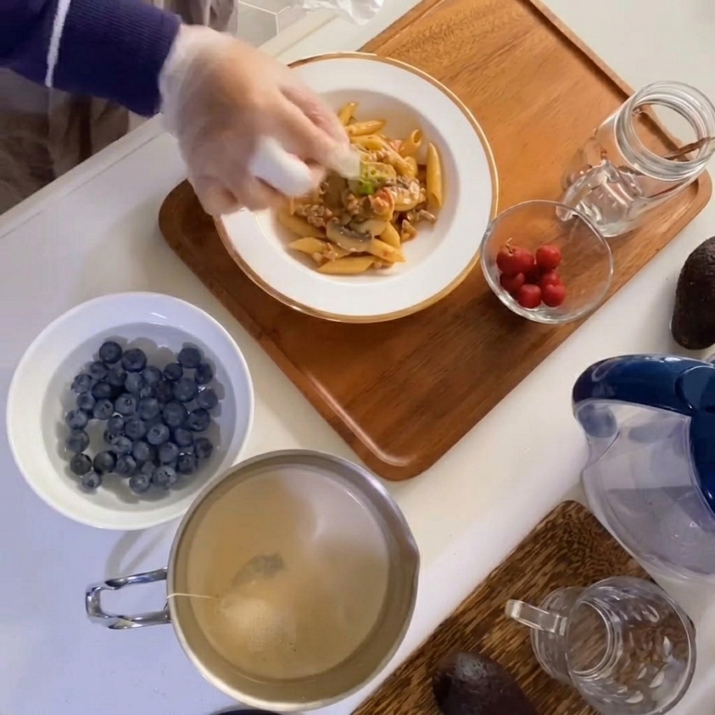 Una mano colocando tomillo fresco sobre un tazón de pasta con champiñones y carne.