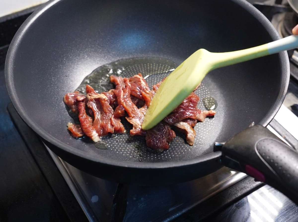 Espátula salteando tiras de ternera parcialmente cocinadas en una sartén.
