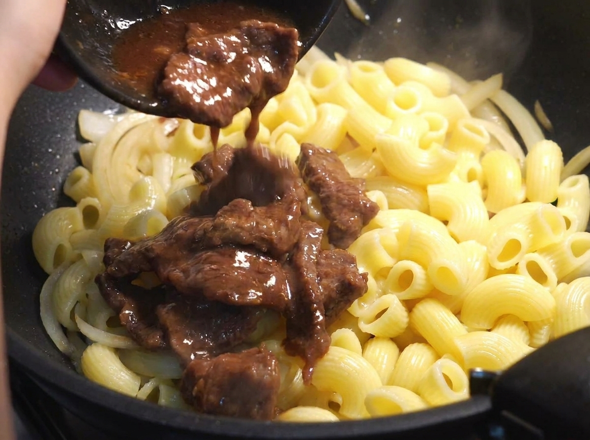 Tiras de ternera añadidas a la sartén con la pasta y las cebollas.