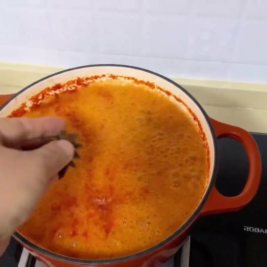 Tres vainas de anís estrellado cayendo en la vibrante y roja sopa de almejas a fuego lento.