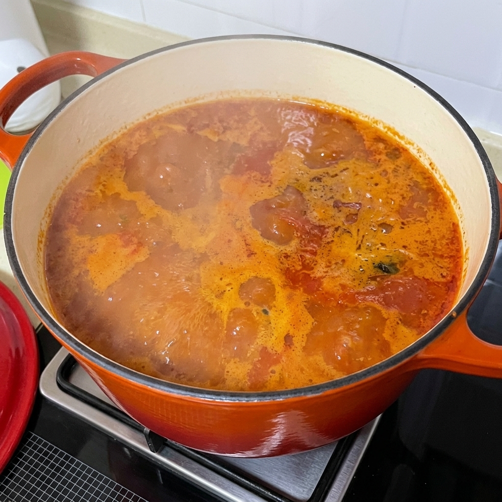 Rodajas de patata recién cortadas añadiéndose a la burbujeante sopa picante de almejas.
