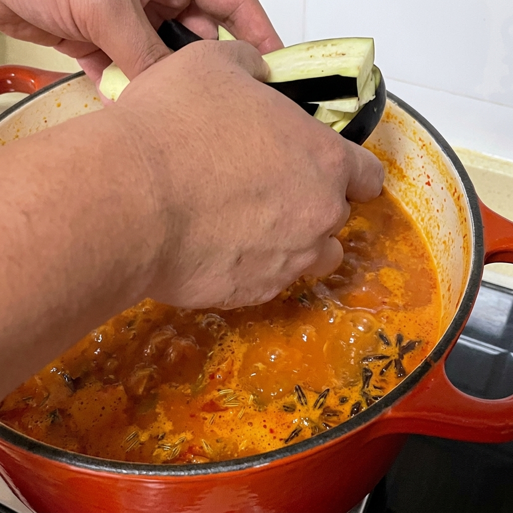 Tiras de berenjena en rodajas añadiéndose a la olla de sopa picante de almejas.