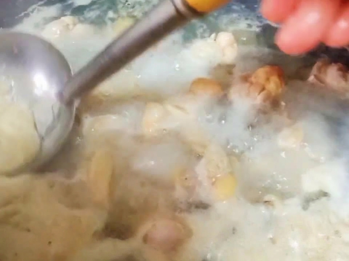 Un cucharón de metal retirando espuma espesa de la superficie de agua hirviendo con pollo.