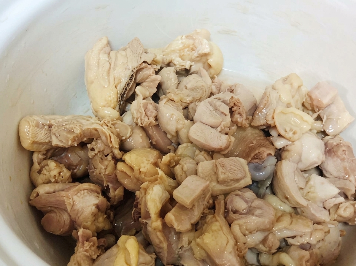 Trozos de pollo blanqueado reposando dentro de una olla de cerámica blanca.