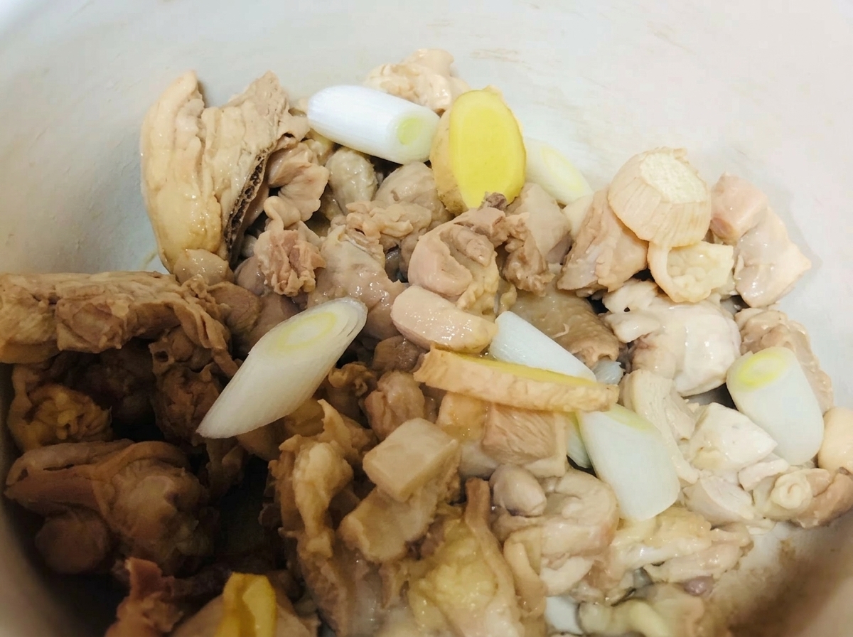 Trozos de pollo en una olla de barro sazonados con cebolletas, jengibre y condimentos líquidos.