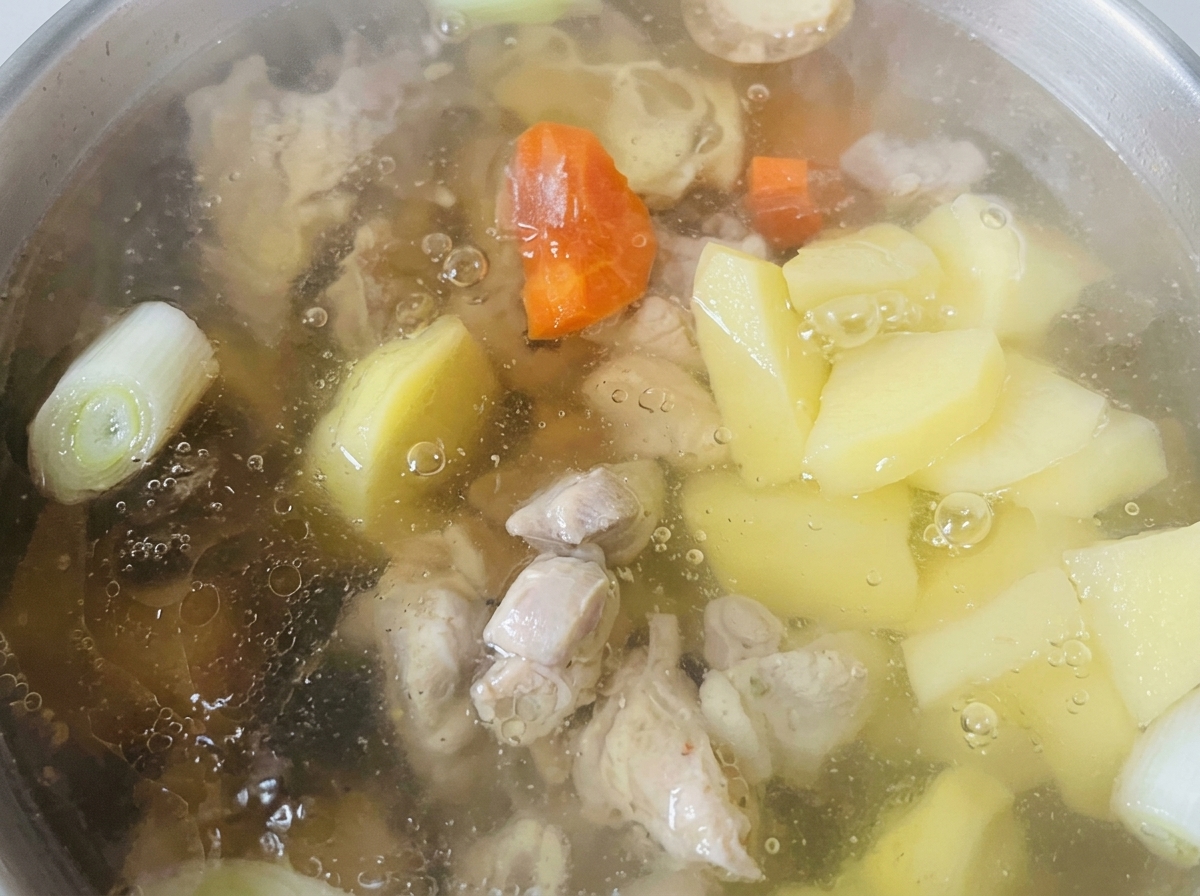 Trozo de zanahoria y patata cocinándose en un caldo claro junto al pollo.