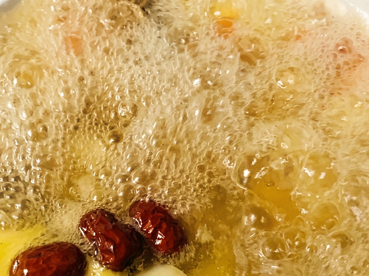 Dátiles rojos y condimentos siendo añadidos a una olla de sopa de pollo hirviendo.