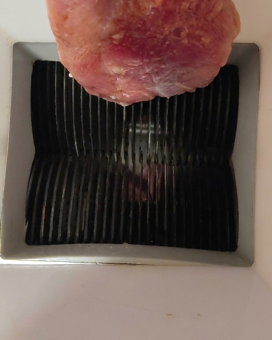 Un trozo de carne de pato cruda siendo introducido en la parte superior de una cortadora de carne.