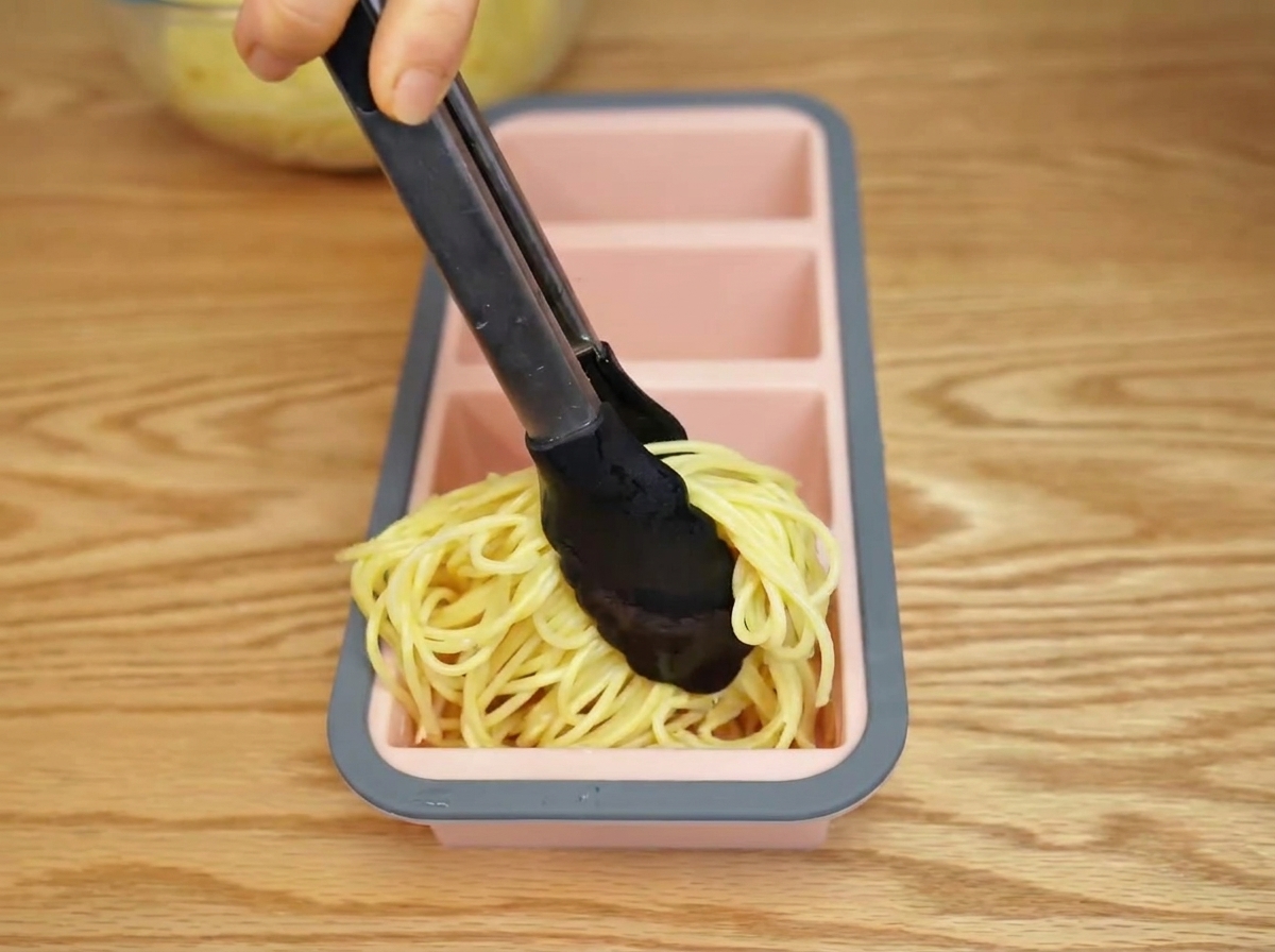Pasta cocida siendo colocada en un molde de silicona con unas pinzas.