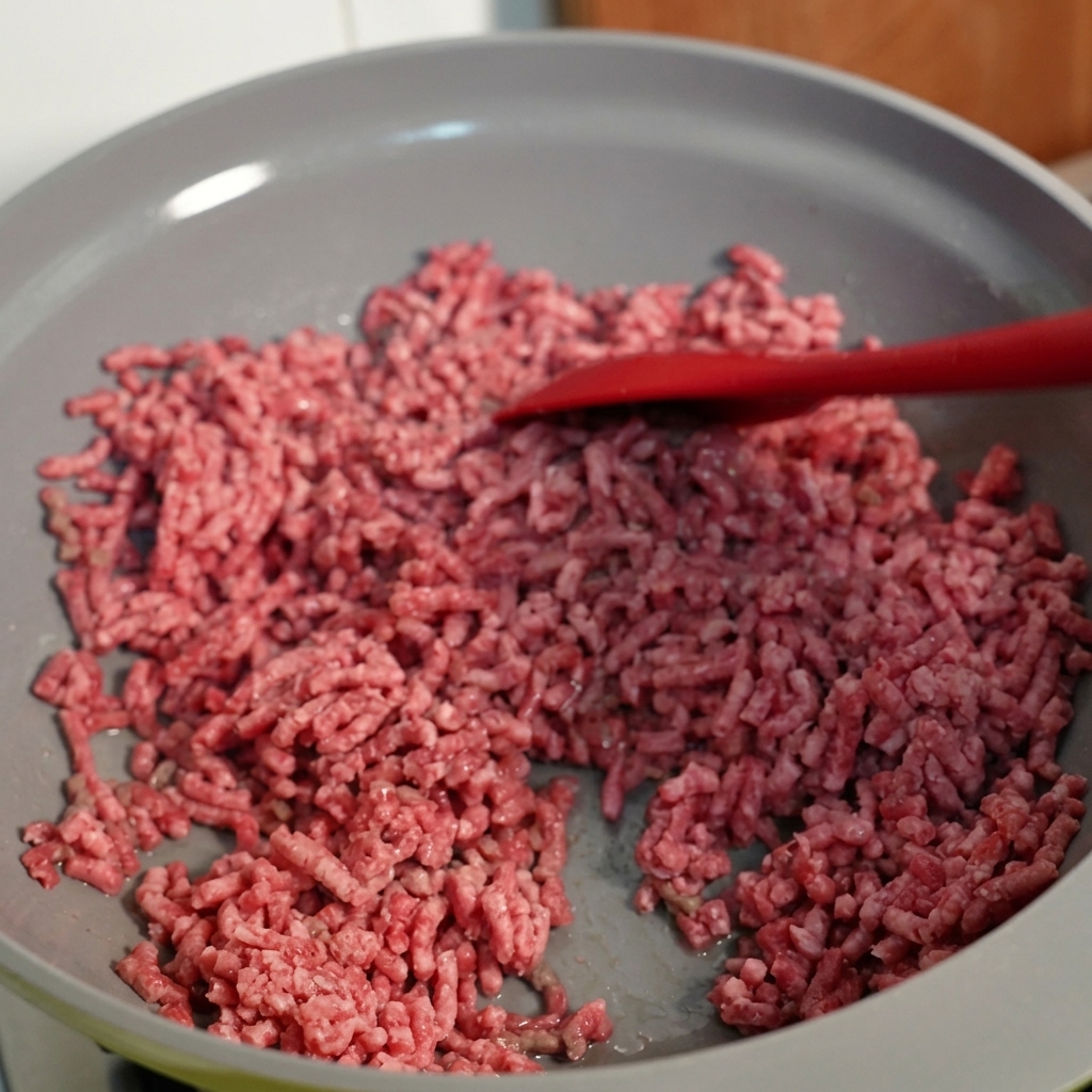 Carne picada siendo removida en una sartén, mostrando una textura dorada.