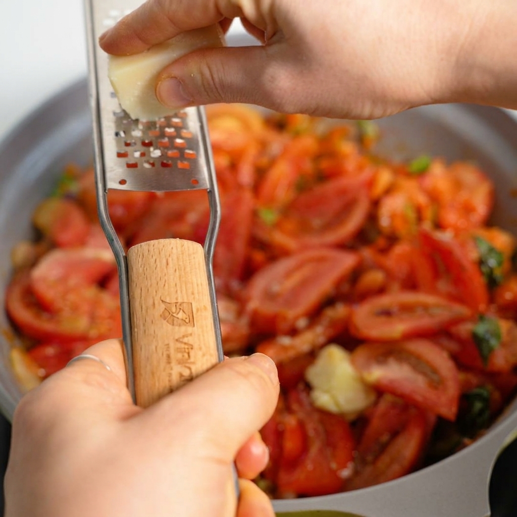 Queso parmesano fresco siendo rallado sobre una salsa de carne y tomate burbujeante en una sartén.