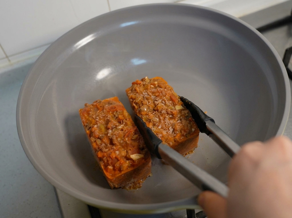 Bloques congelados de pasta y salsa de carne siendo calentados en una sartén con pinzas.