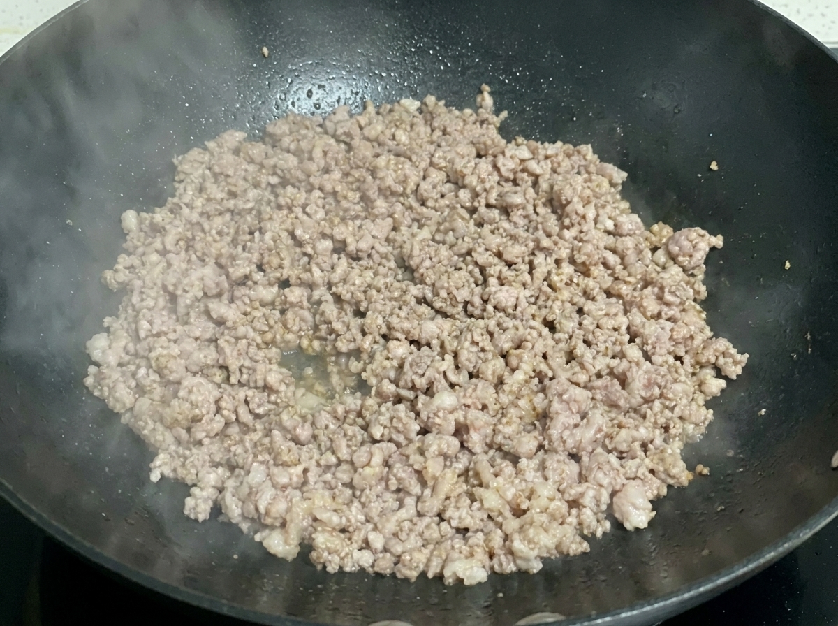Migas de carne de cerdo picada cocinadas y ligeramente doradas chisporroteando en un wok oscuro.