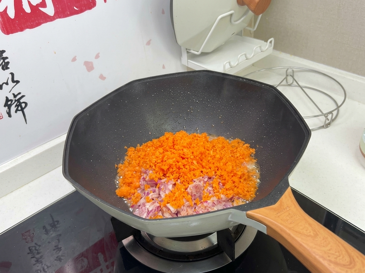 Un montón colorido de zanahorias naranjas y cebollas moradas picadas finamente cocinándose en un wok caliente.
