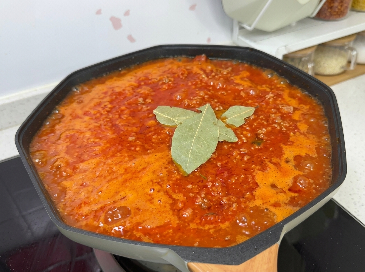 Una salsa de carne y tomate hirviendo a fuego lento en un wok, sazonada con sal, azúcar, hojas de laurel y pimienta negra.