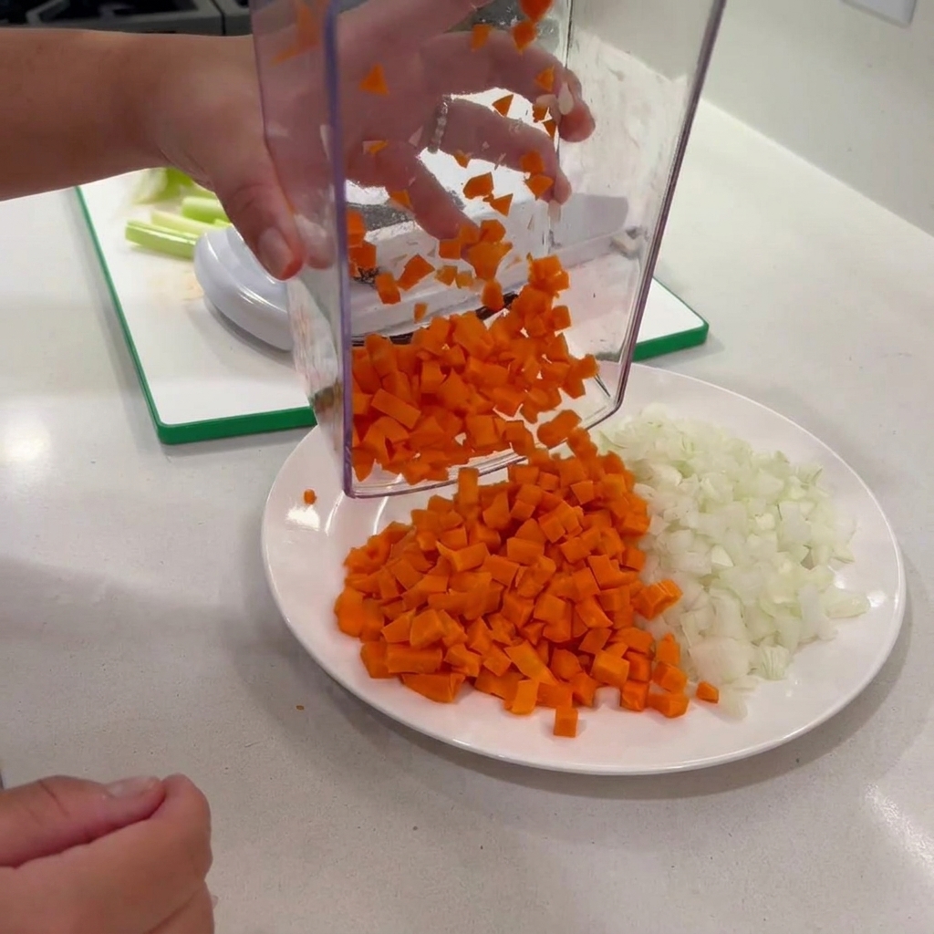 Zanahorias picadas dispensadas de un picador transparente a un plato con cebollas.