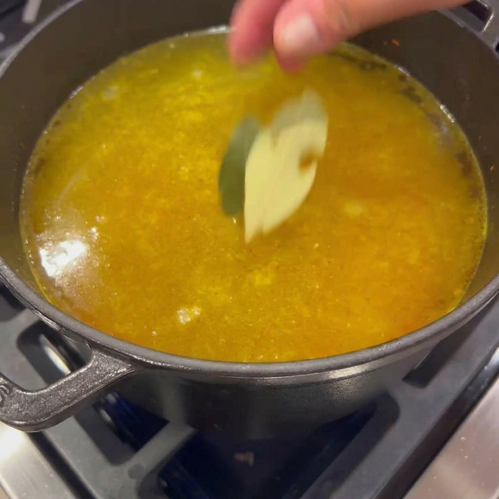 Dos hojas de laurel secas cayendo en una olla de caldo de verduras dorado a fuego lento.