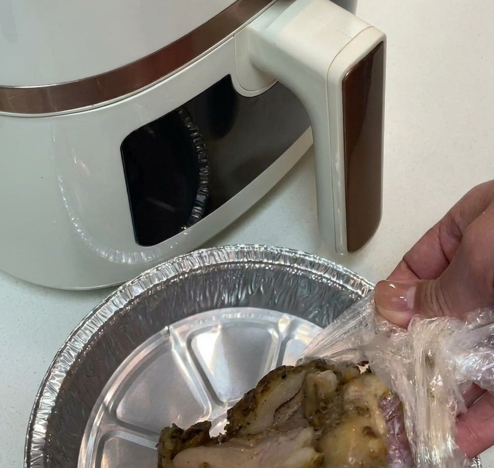 Muslos de pollo sazonados en una cesta de air fryer con papel de aluminio.