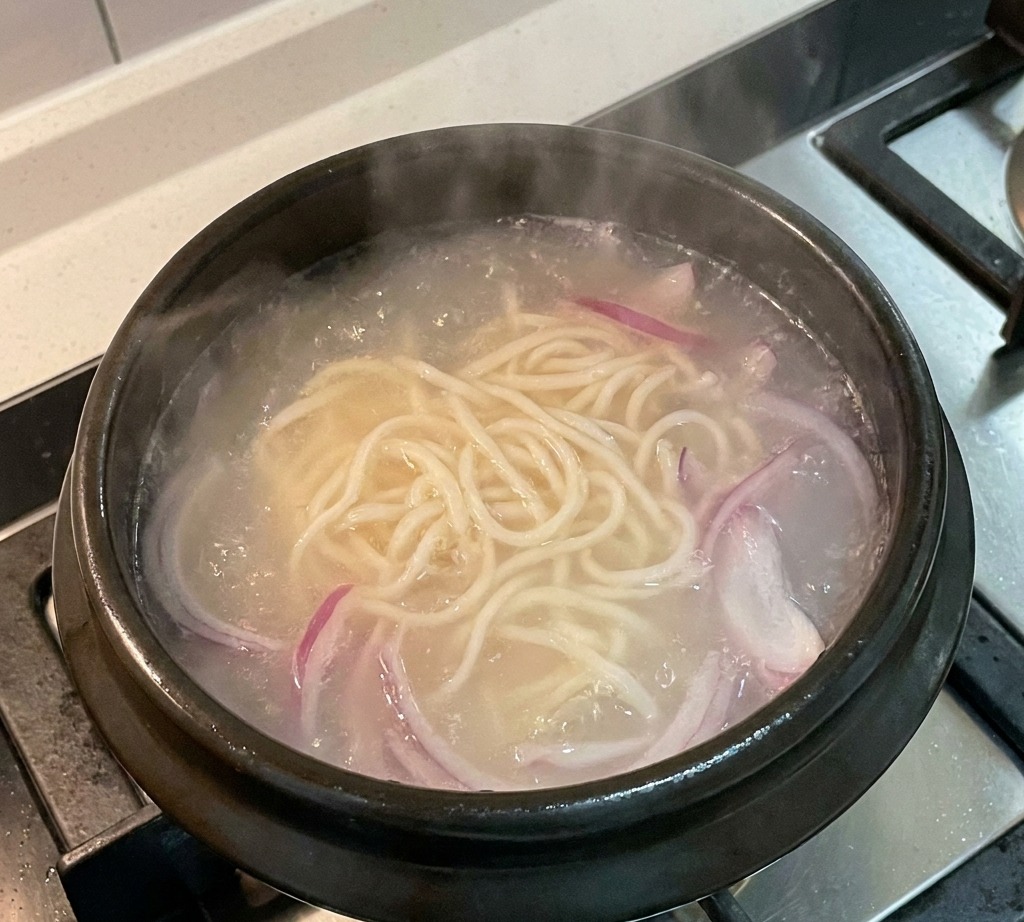 Cebolla roja cocinándose en el caldo con fideos.