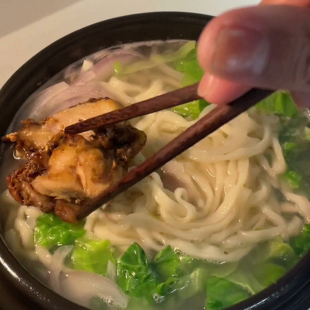 Trozos de pollo colocados sobre los fideos en el cuenco.