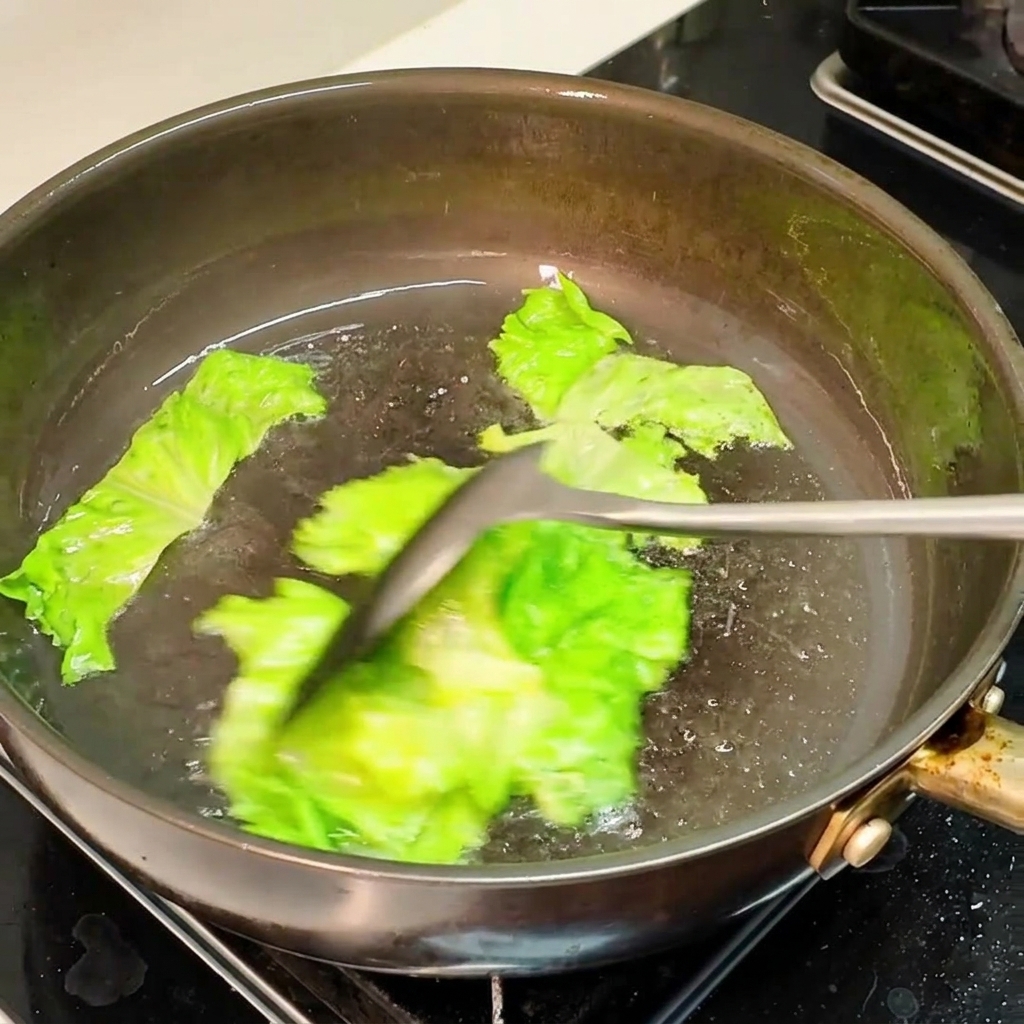 Trozos de lechuga verde salteándose en una sartén caliente con aceite usando una espátula.