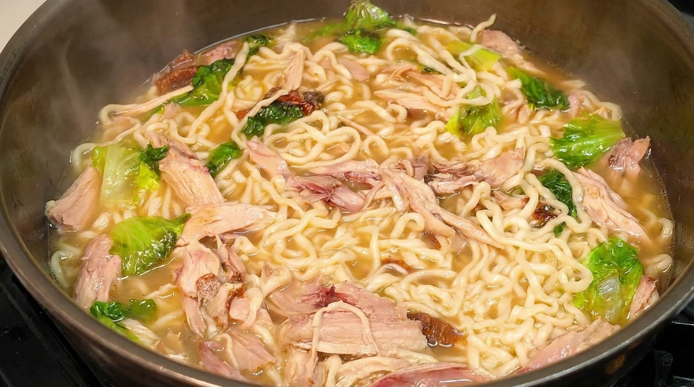 Una olla humeante de sopa de fideos con pollo, fideos ondulados, pollo a la pimienta desmenuzado y lechuga fresca.