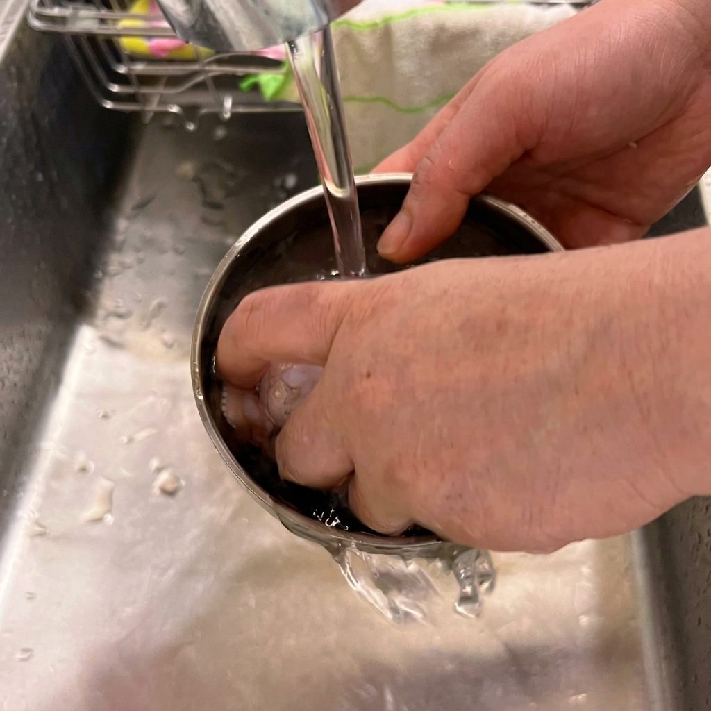 Alitas de pollo frescas siendo lavadas en un bol de acero inoxidable bajo el grifo de la cocina.