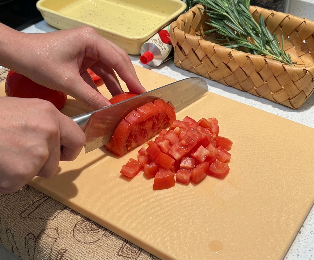 Tomates frescos pelados siendo picados en trozos pequeños y uniformes.
