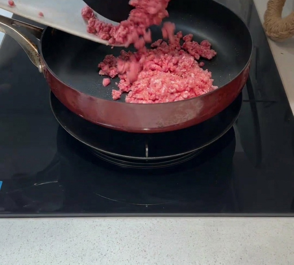 Carne picada cruda siendo añadida a una sartén caliente con un poco de aceite.