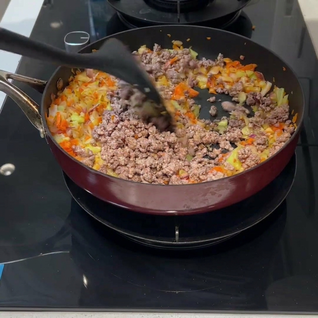 Carne picada y vegetales mezclados en una sartén con una espátula.