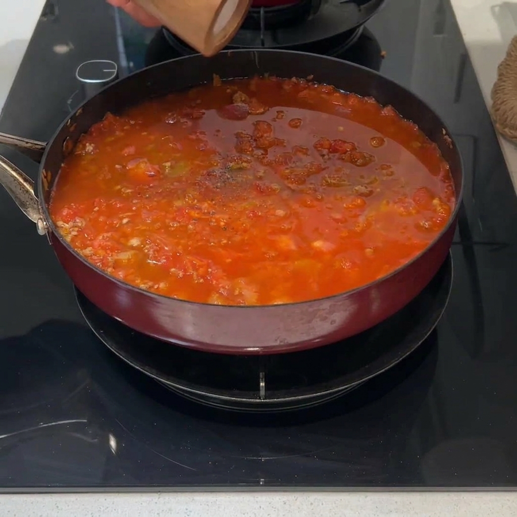 Una ramita de romero fresco sobre una salsa roja que hierve a fuego lento.