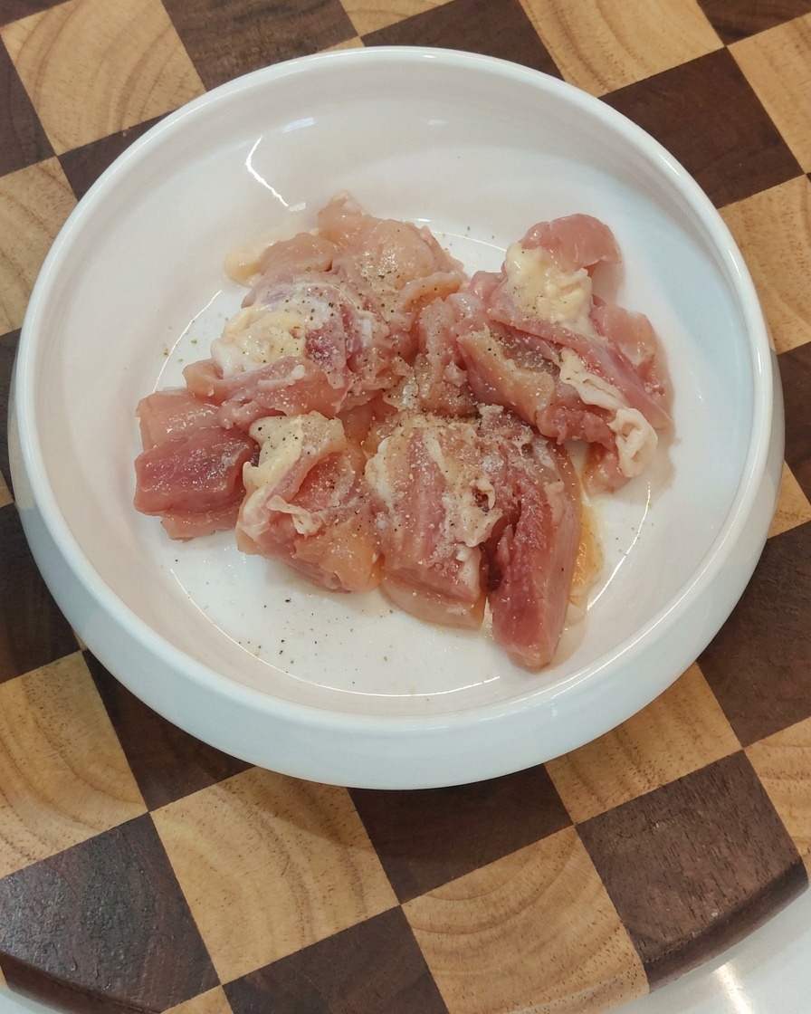 Tazón que contiene trozos de pollo crudo sazonados listos para la sartén.