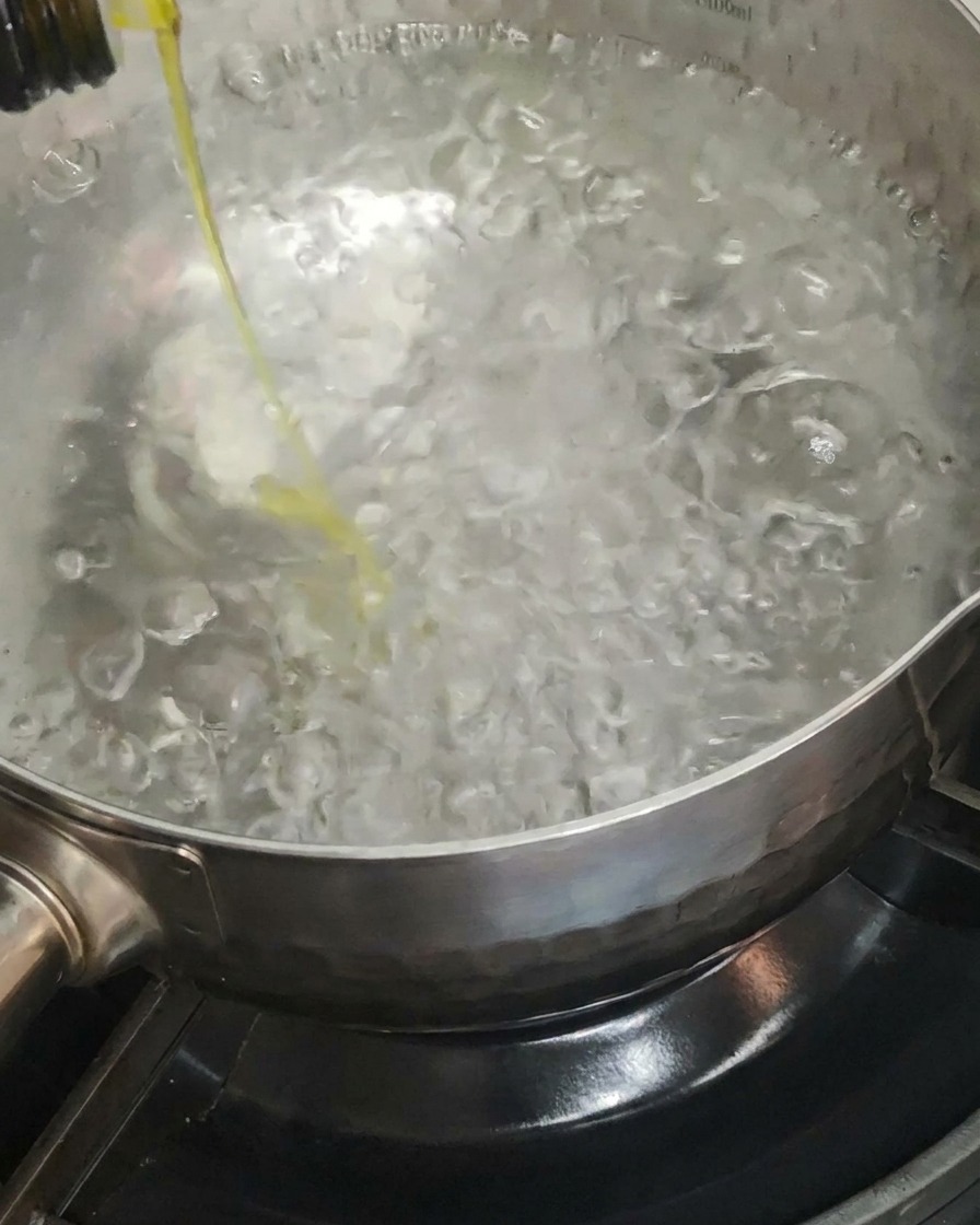 Aceite de oliva siendo vertido en una olla grande con agua hirviendo.