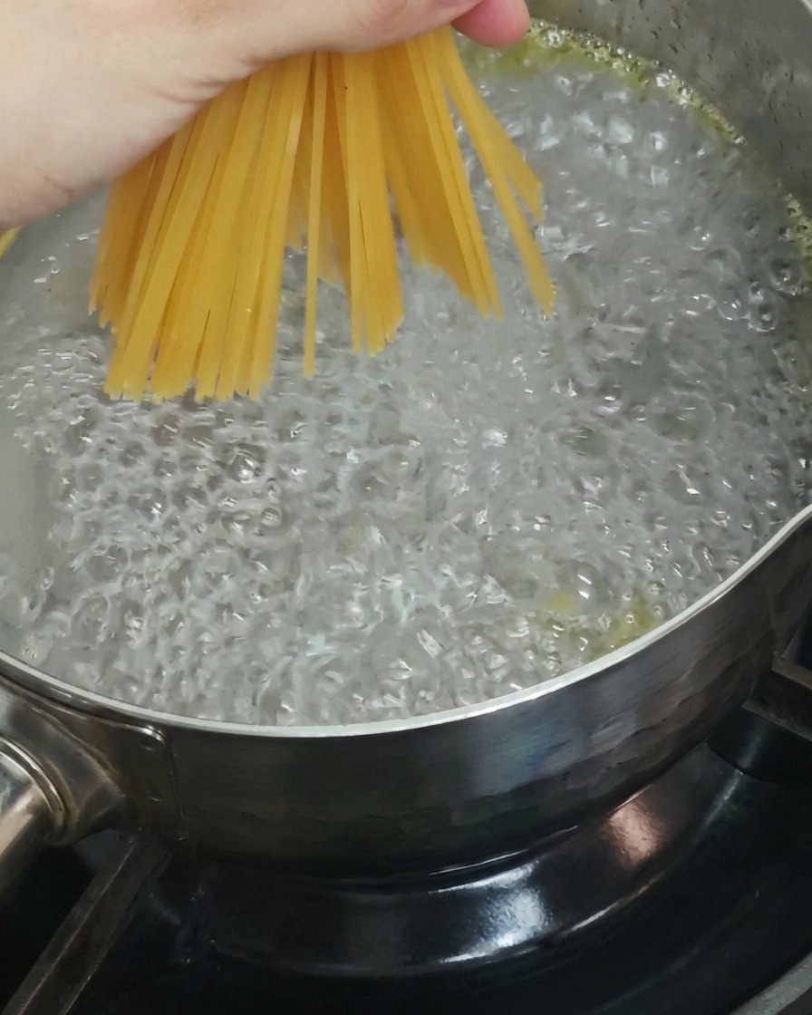Primer plano de una mano sosteniendo un manojo de fideos de espagueti secos y bajándolos a una olla de agua hirviendo burbujeante.