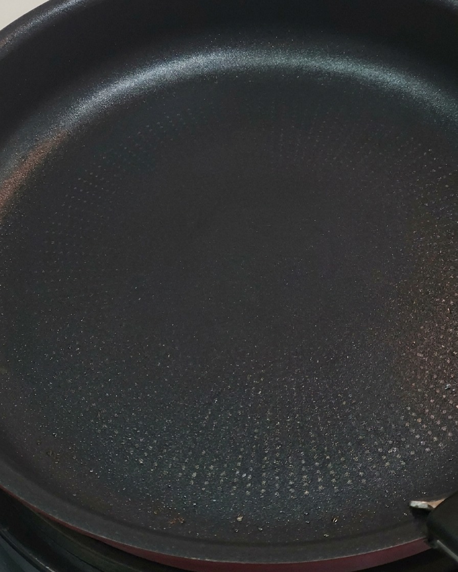 Pinzas rojas volteando trozos de pollo en una sartén, mostrando algunas superficies doradas.