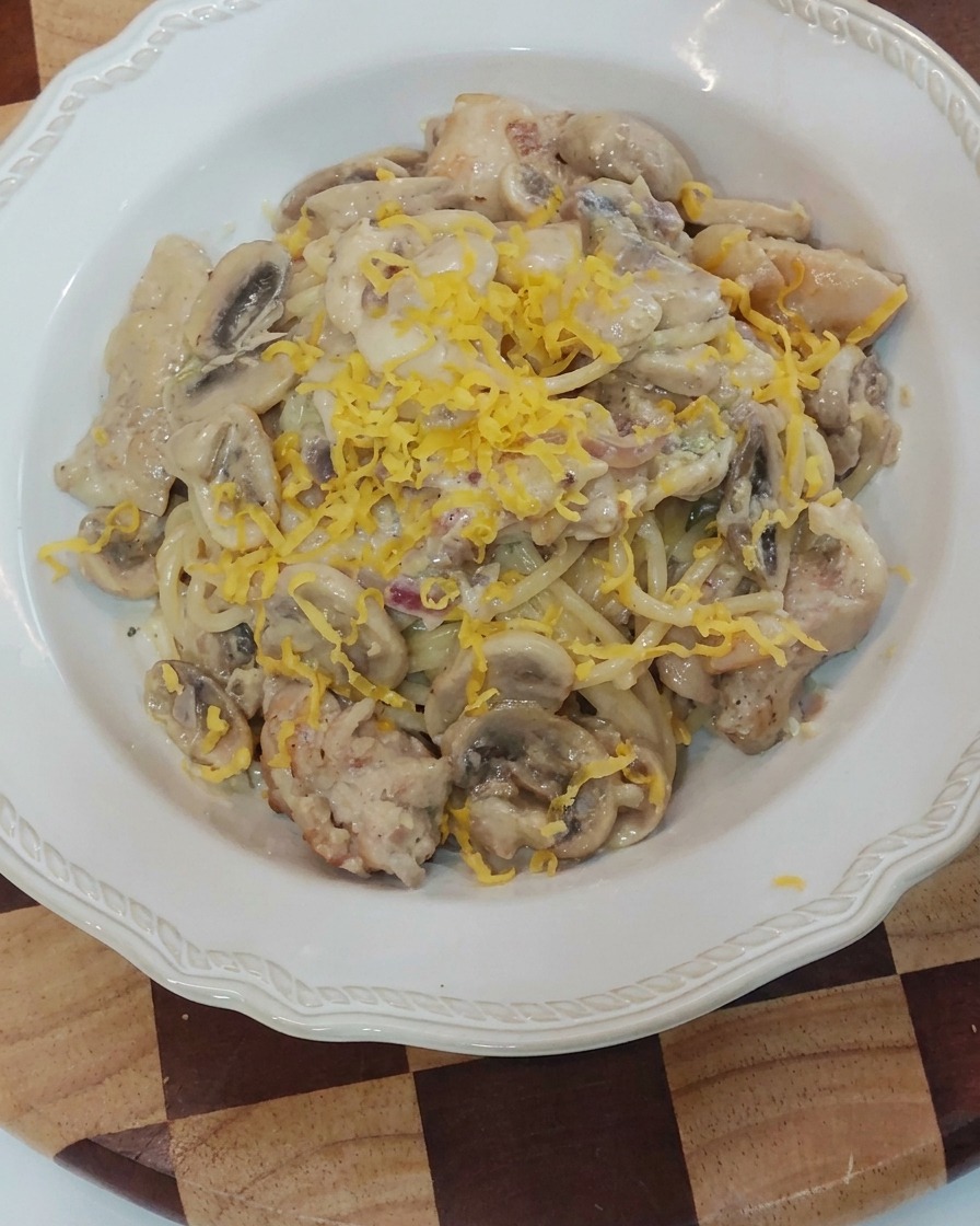 Un bloque de queso amarillo siendo rallado sobre la pasta cremosa emplatada.