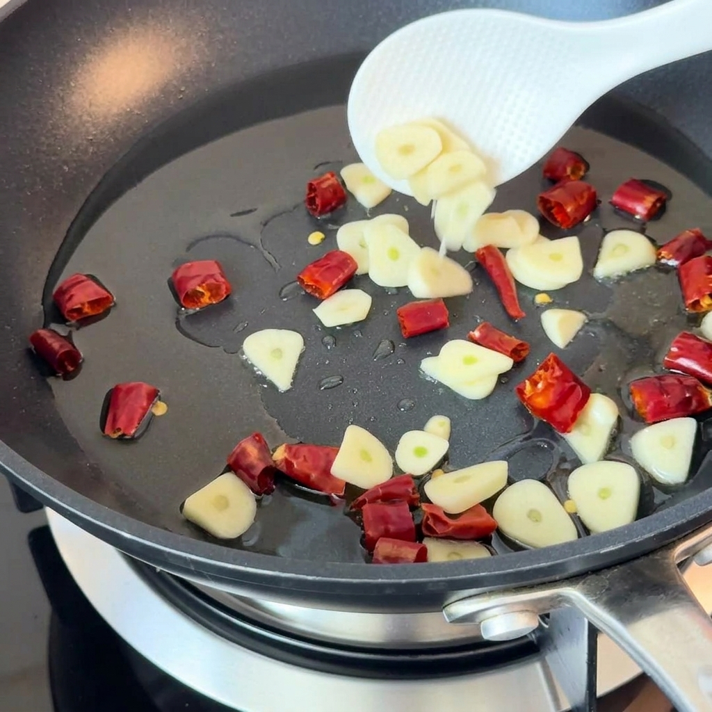 Ajo en rodajas y chiles secos salteándose en aceite caliente en una sartén.