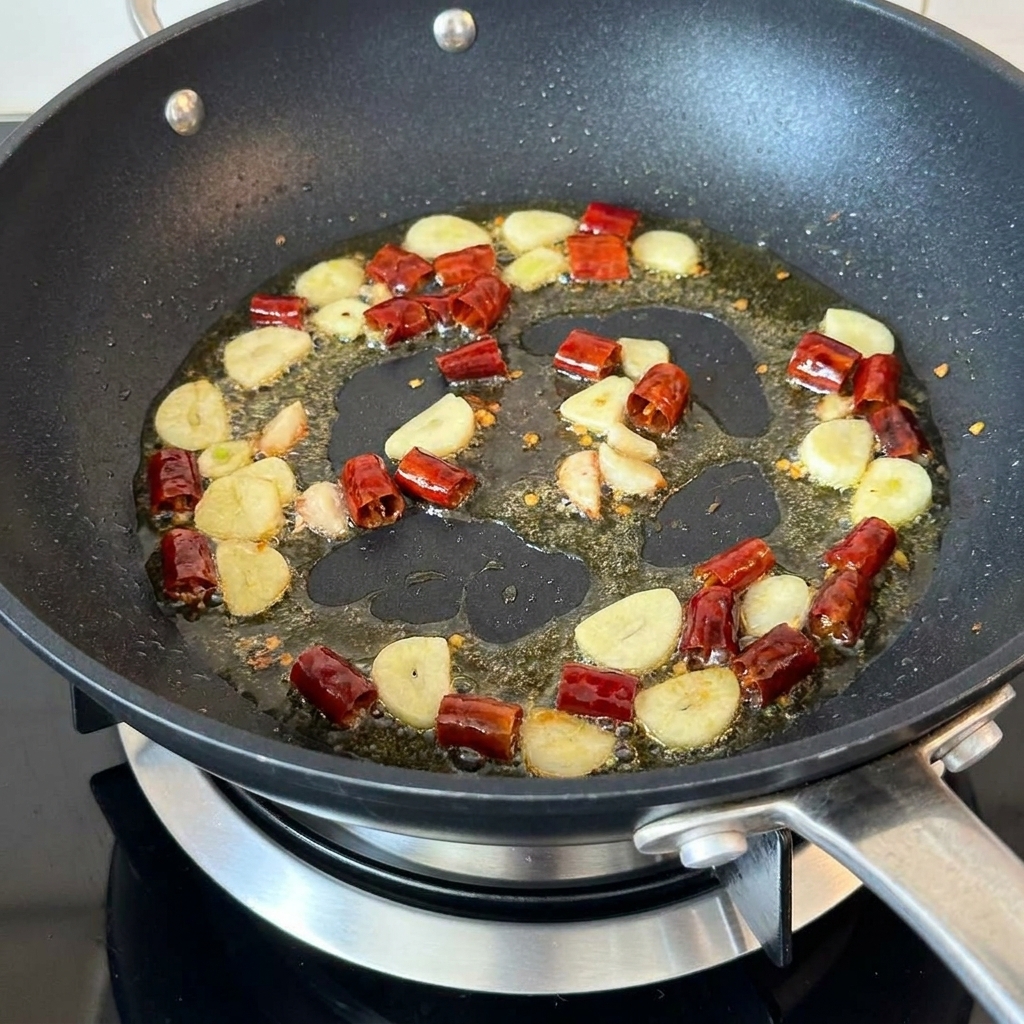 Champiñones picados salteándose con ajo y chiles secos en una sartén.