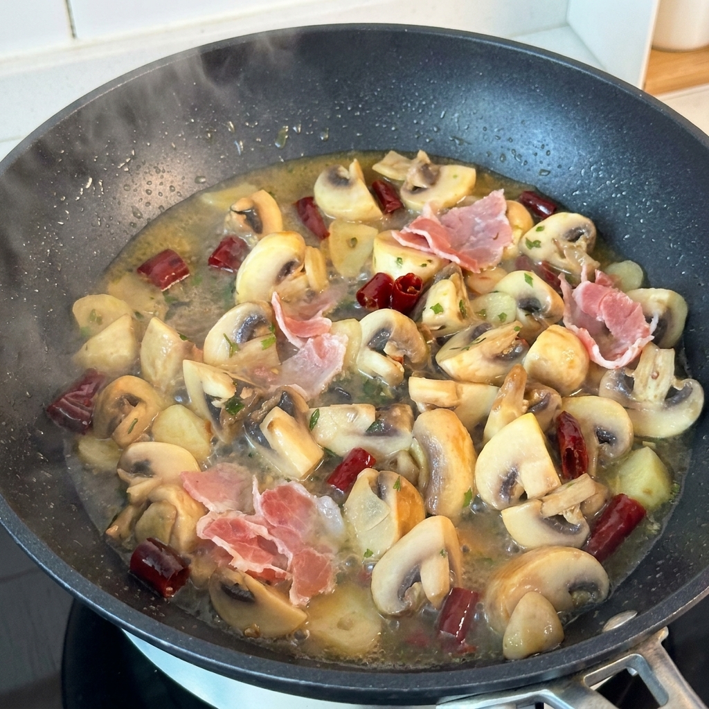Trozos de jamón curado rosado en una sartén caliente junto a champiñones cocidos y salsa de mantequilla.