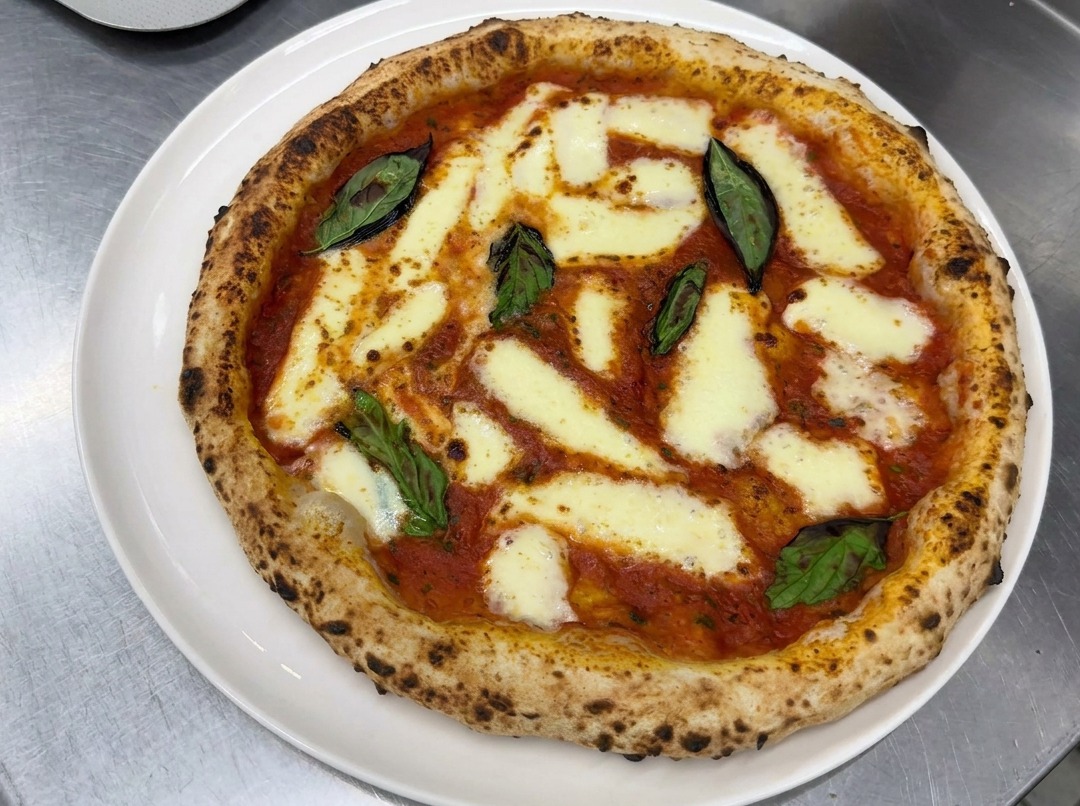 Manos estirando cuidadosamente una bola de masa de pizza fermentada sobre una encimera enharinada hasta formar una corteza redonda perfecta.