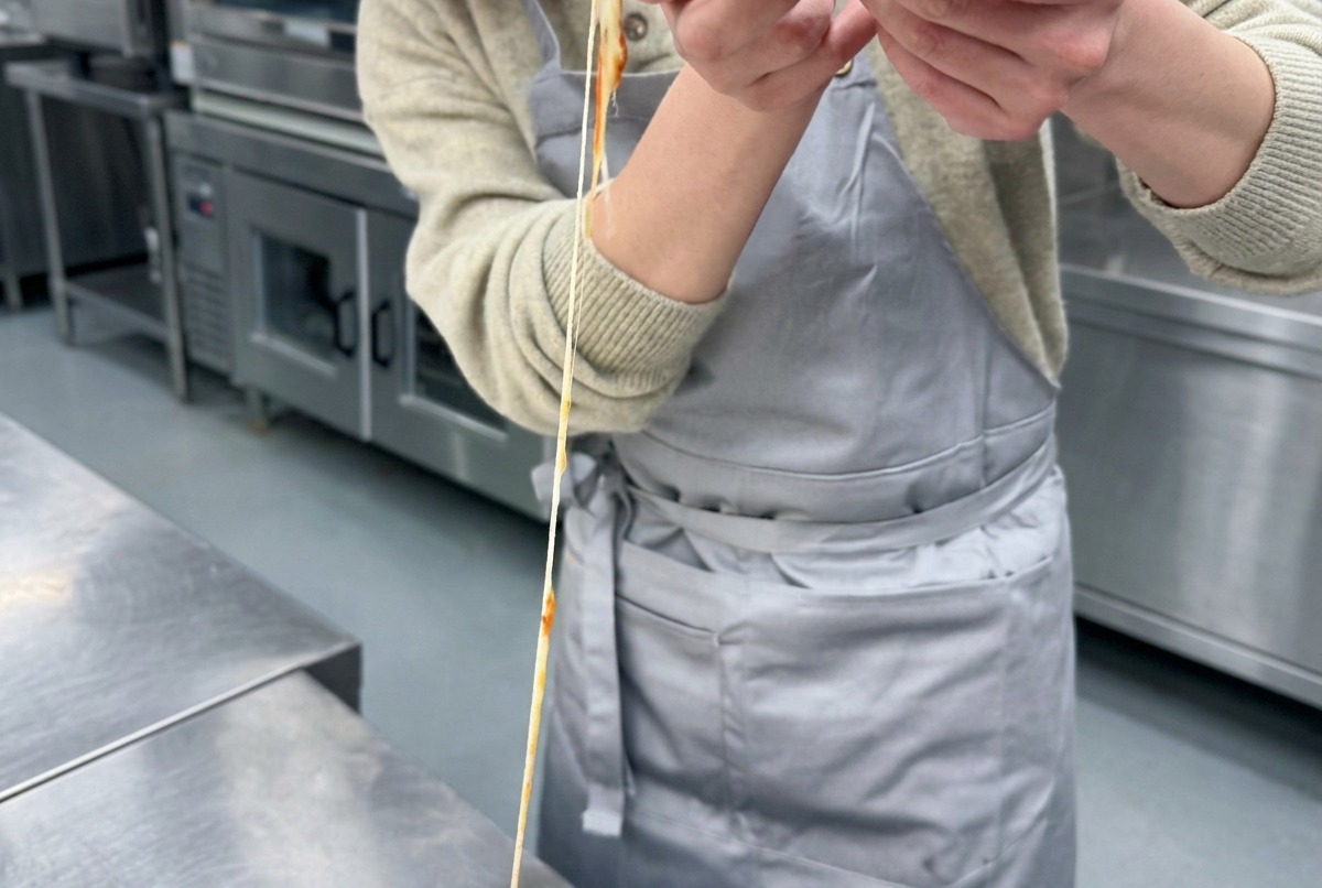 Un cucharón extendiendo salsa de tomate roja vibrante en un movimiento circular sobre el centro de una base de masa de pizza cruda.