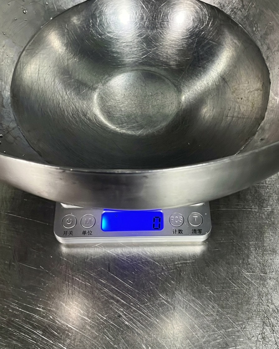 Un tazón grande de acero inoxidable con agua sobre una báscula de cocina digital.