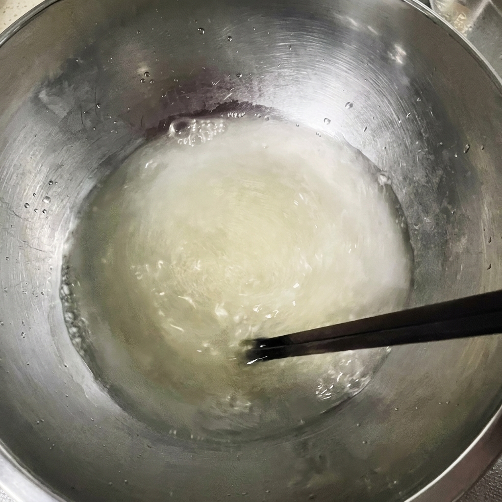 Mezcla de agua, levadura y sal siendo agitada con palillos en un tazón de metal.