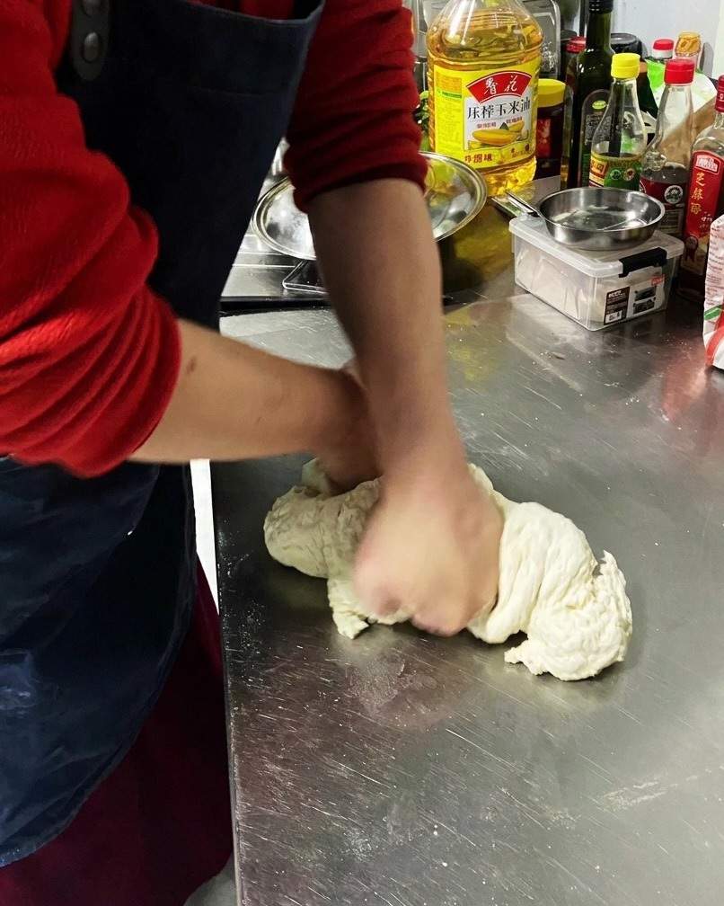 Primer plano de masa siendo amasada sobre una superficie metálica.