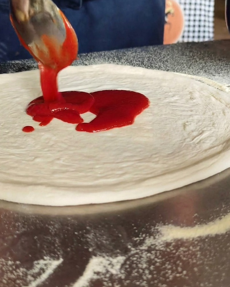 Salsa de tomate siendo extendida con una cuchara sobre la base de la pizza.