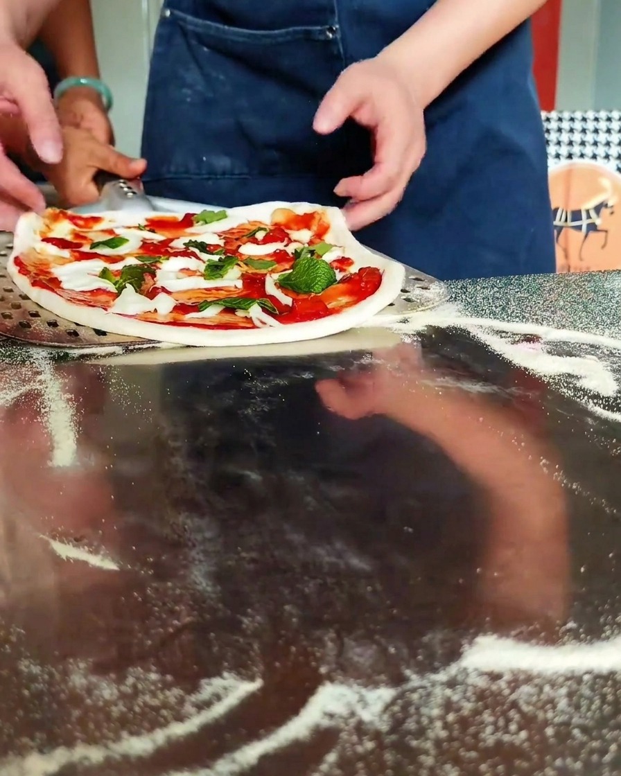 Manos colocando la pizza sobre una pala metálica perforada.