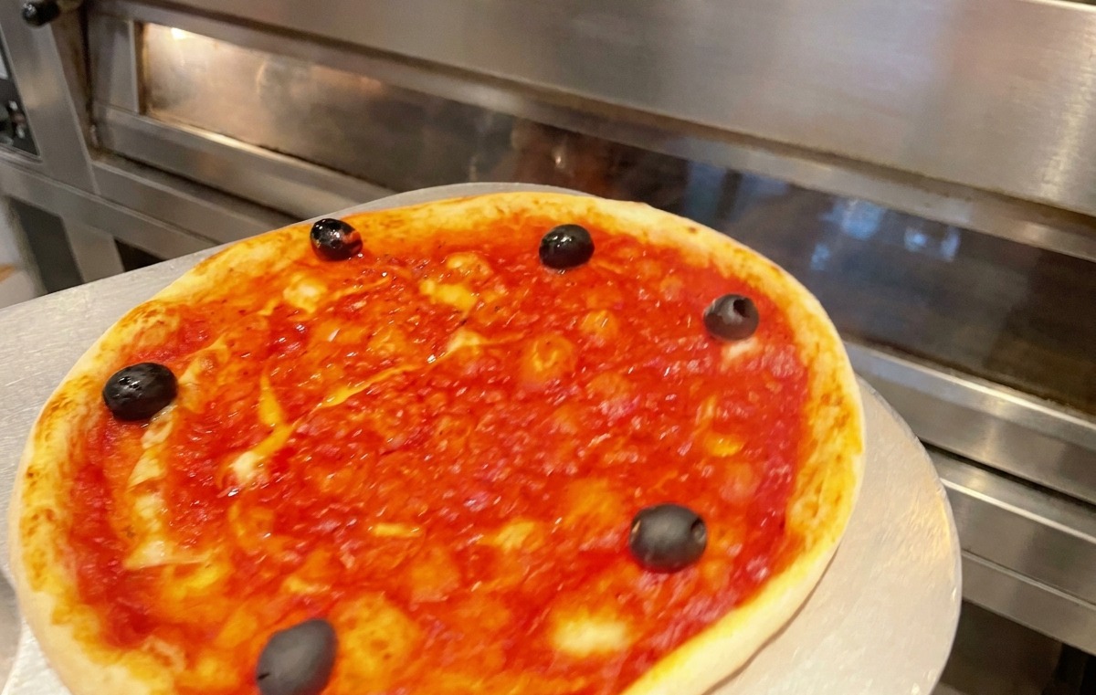 Una bandeja de pizza siendo introducida en un horno comercial caliente para hornear.