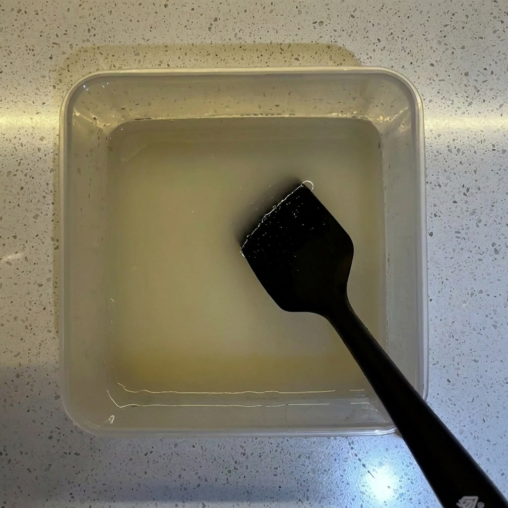 Harina vertiéndose en un recipiente transparente que contiene la mezcla preparada de agua y levadura.
