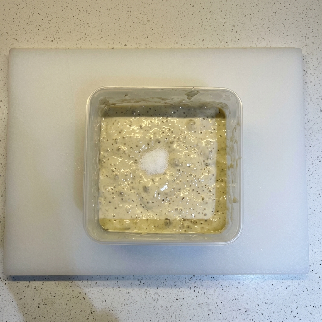Sal y un montón de harina sobre una mezcla de masa fermentada y burbujeante en un recipiente cuadrado.
